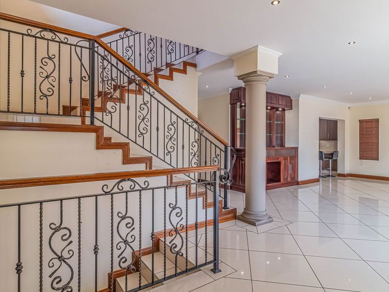 Spacious entrance hall featuring a grand staircase with wrought iron railings, polished tiled flooring, and a decorative column leading into an open living area.
