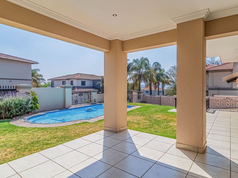 A spacious covered patio featuring tiled flooring and recessed lighting, overlooking a private swimming pool and landscaped garden area.