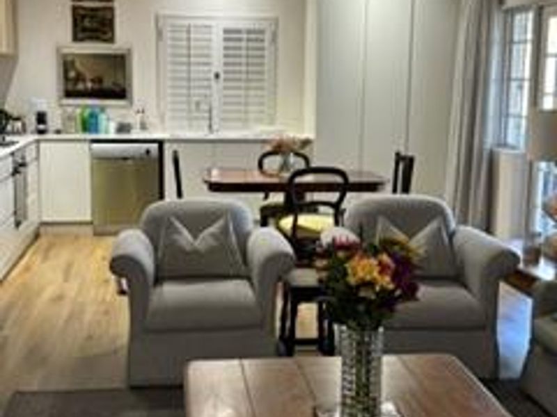 An open-plan living and kitchen area featuring modern cabinetry, recessed lighting, plantation shutters, and hardwood flooring in a well-maintained cottage setting.