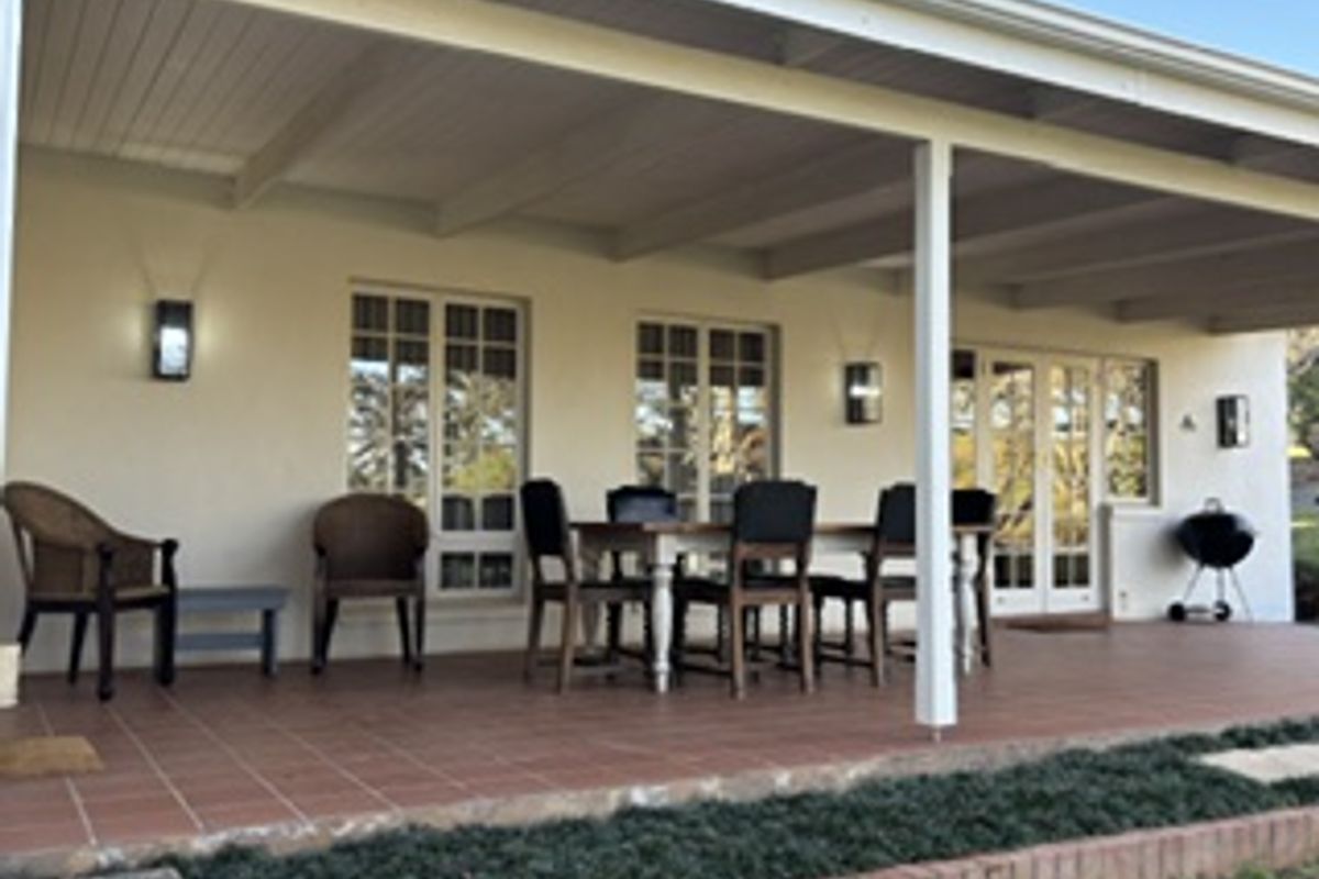 A spacious covered patio featuring tiled flooring, wall-mounted lighting, and direct access to the interior through classic french doors.