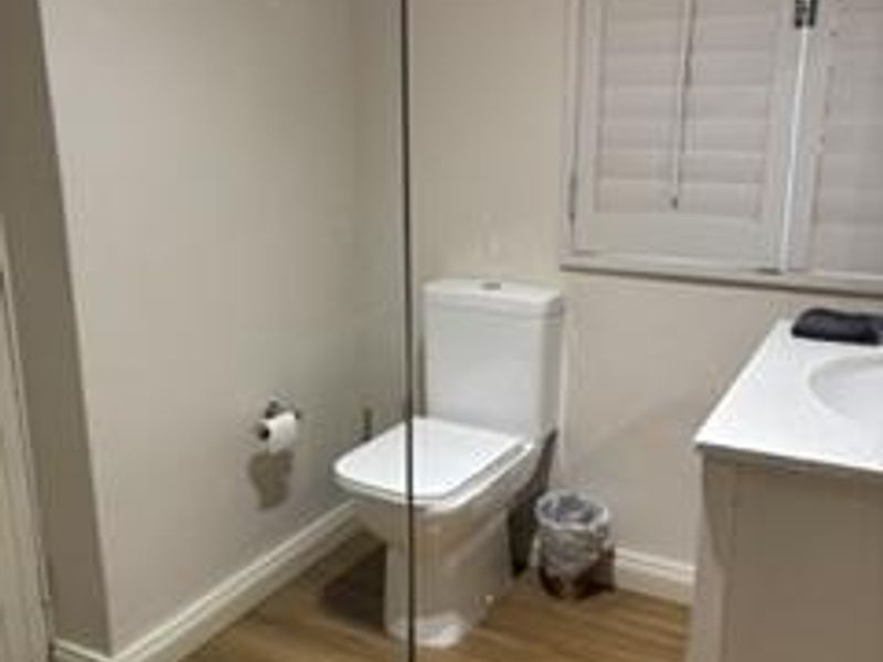 A clean, modern bathroom featuring a white toilet, vanity with basin, and plantation shutters, finished with light timber-look flooring.
