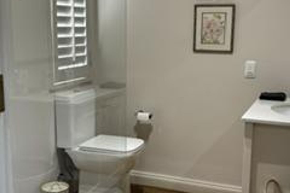 A well-maintained bathroom featuring a modern toilet, vanity unit, shutter blinds, and wood-look laminate flooring.
