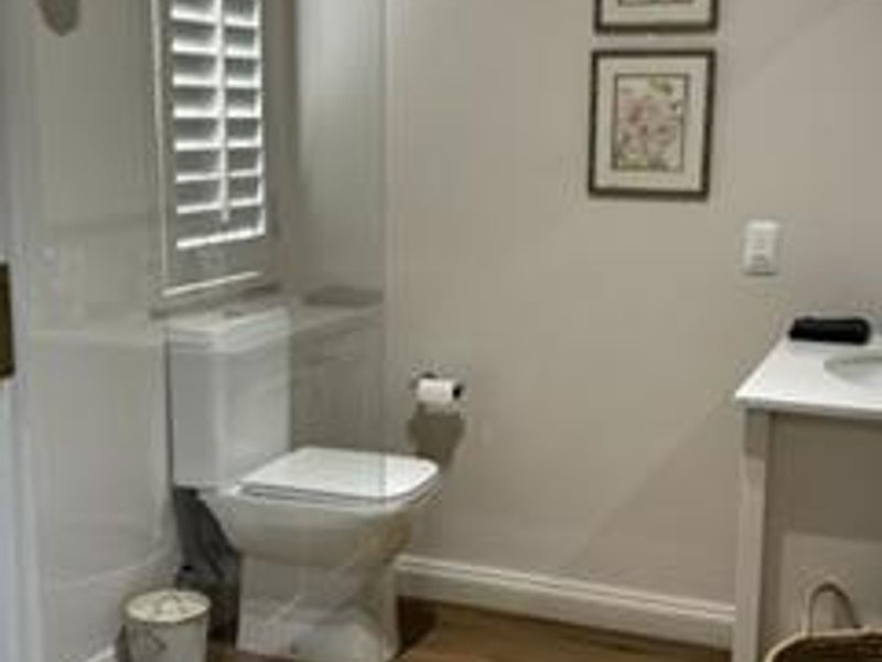 A well-maintained bathroom featuring a modern toilet, vanity unit, shutter blinds, and wood-look laminate flooring.