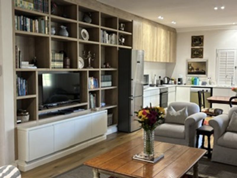 Open plan living and kitchen area featuring extensive built-in timber shelving, modern cabinetry, recessed lighting, and high-quality hardwood flooring.