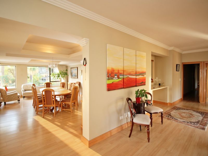 Spacious open-plan living and dining area featuring laminate flooring, a stone fireplace, and elegant recessed ceiling details with crown molding.