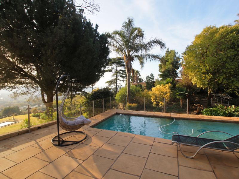 Outdoor pool area featuring stone paving, a glass balustrade, and established garden surroundings with scenic views.