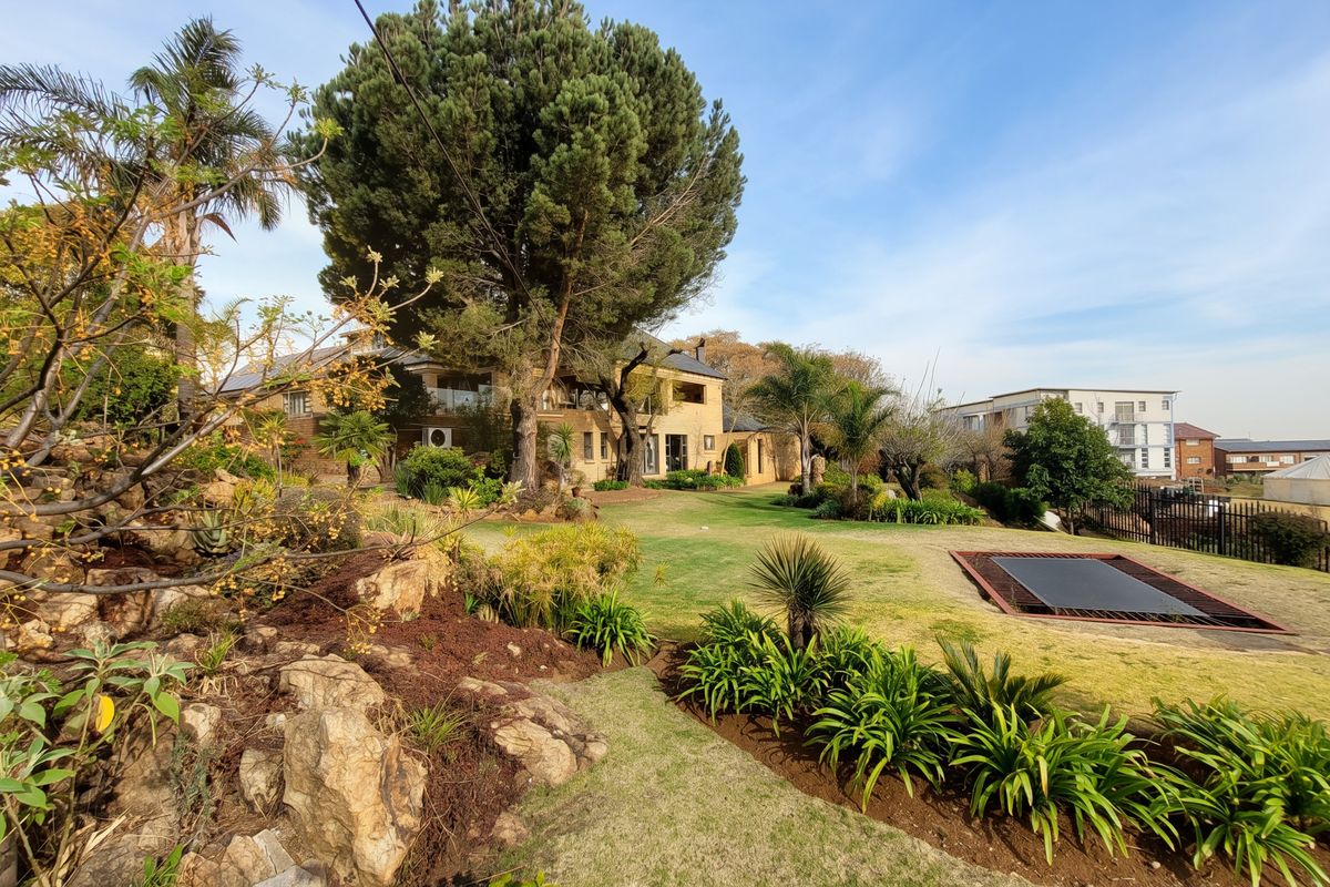A spacious rear garden featuring a well-maintained lawn, mature trees, stone landscaping, and an integrated in-ground trampoline.