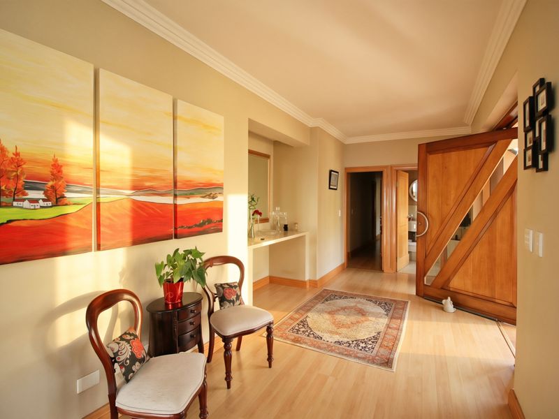 Welcoming entrance hall featuring warm laminate flooring, crown molding, and a distinctive timber front door.