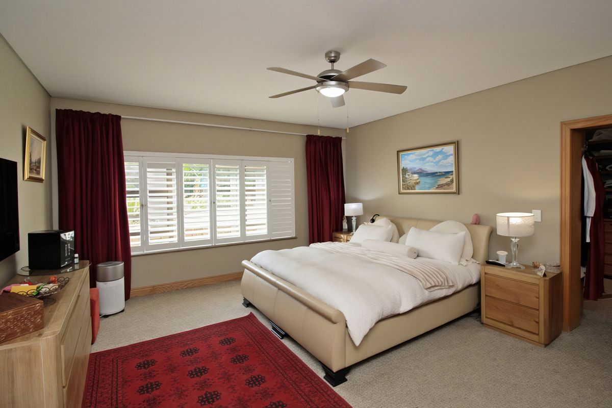 A well-maintained bedroom featuring neutral walls, carpet flooring, a ceiling fan, and plantation shutters, with an adjacent walk-in closet.