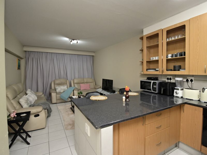 Open-plan living area featuring a functional kitchen with granite countertops and wooden cabinetry, seamlessly flowing into a comfortable lounge space.