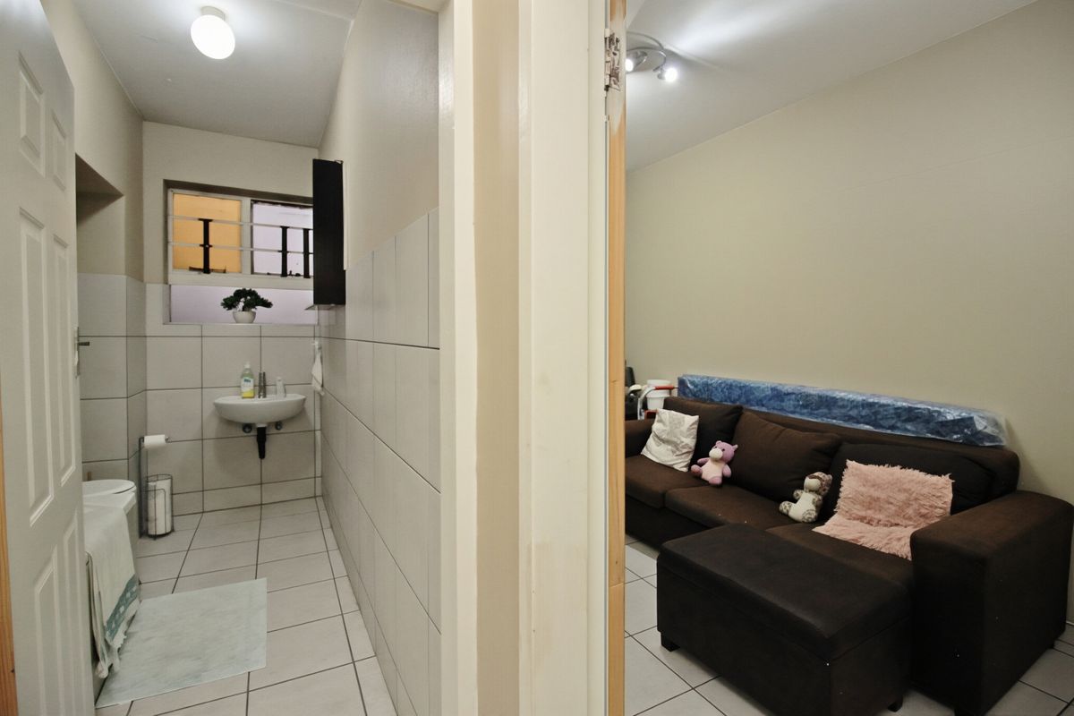 A functional bathroom featuring tiled walls and flooring, a wall-mounted basin, and a toilet, with a window fitted with security bars.