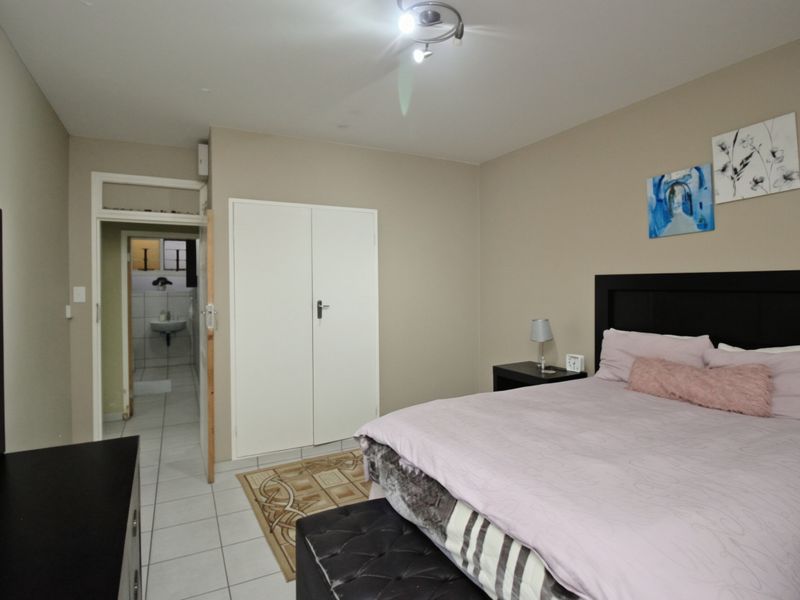 A bedroom featuring tiled flooring, a built-in wardrobe, and an adjoining bathroom, providing a functional and neutral living space.