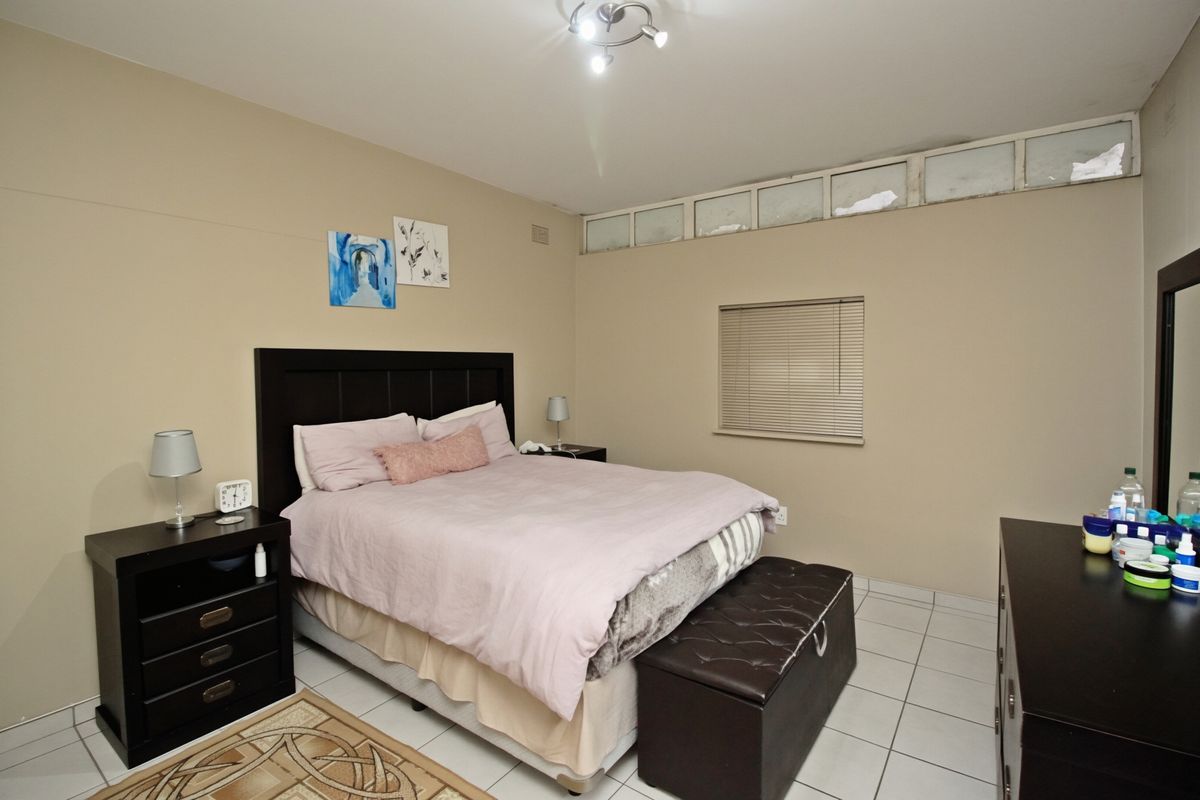 A bedroom featuring tiled flooring and clerestory windows with venetian blinds, providing natural light and a neutral color palette.