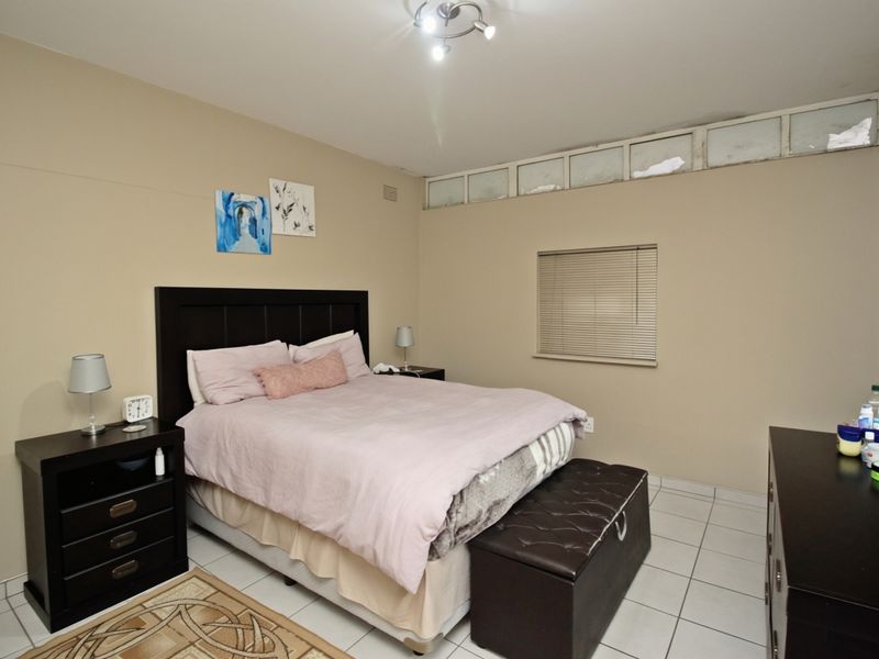 A bedroom featuring tiled flooring and clerestory windows with venetian blinds, providing natural light and a neutral color palette.