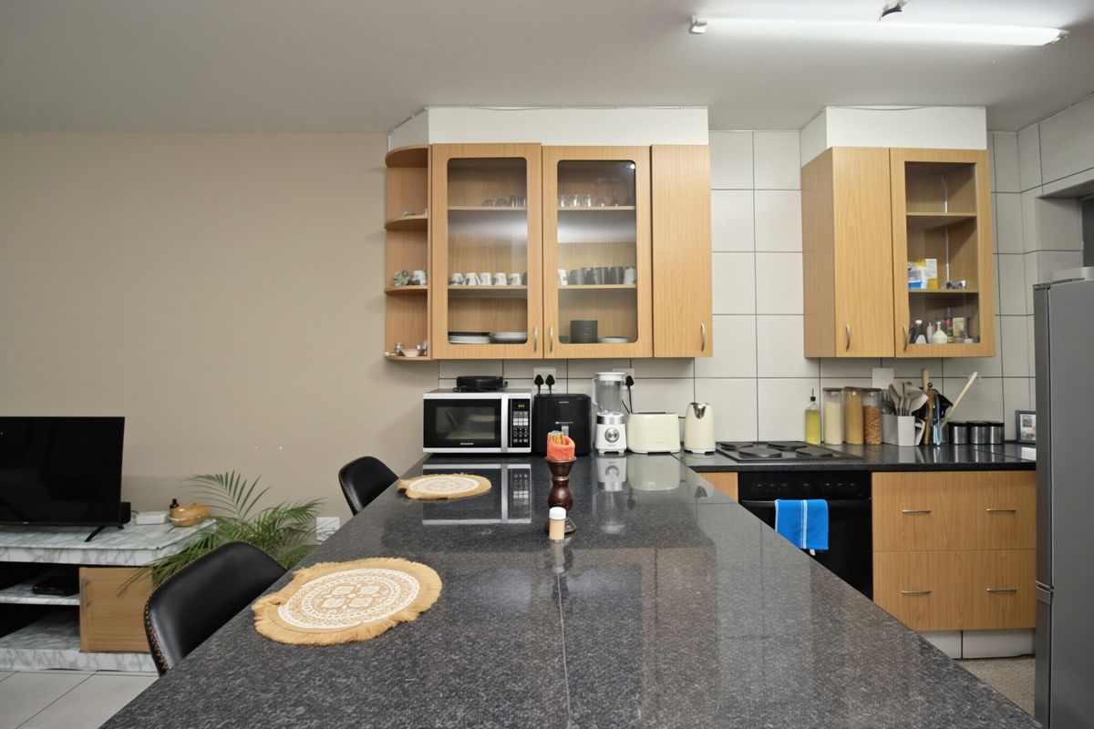 A functional kitchen featuring granite countertops, light wood cabinetry with glass-front uppers, and a tiled backsplash, providing ample workspace and storage.