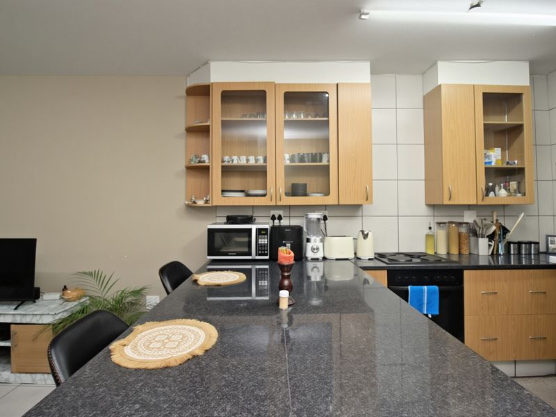 A functional kitchen featuring granite countertops, light wood cabinetry with glass-front uppers, and a tiled backsplash, providing ample workspace and storage.