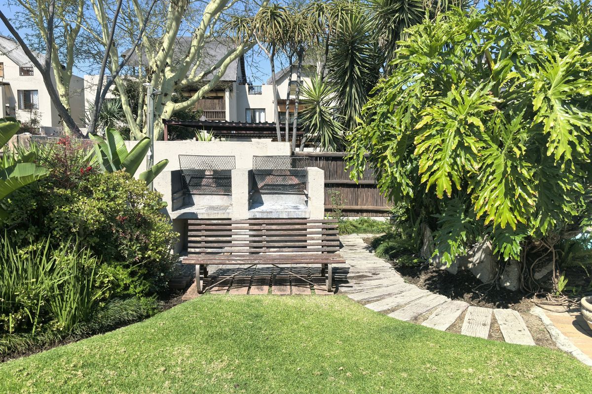 A private rear garden area featuring a built-in double braai, stone pathway, and established greenery, providing a functional outdoor entertainment space.