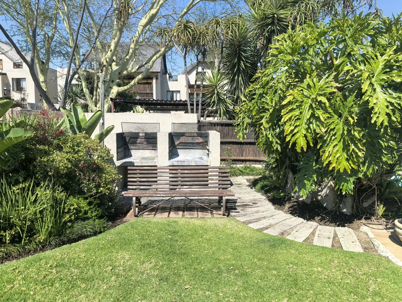 A private rear garden area featuring a built-in double braai, stone pathway, and established greenery, providing a functional outdoor entertainment space.