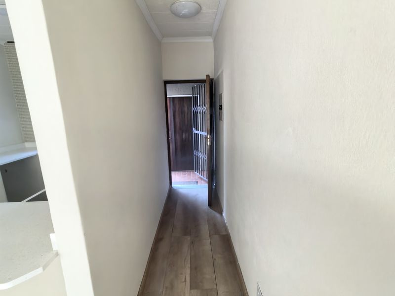 A clean, neutral-toned hallway featuring modern laminate wood-look flooring and a security gate at the entrance.