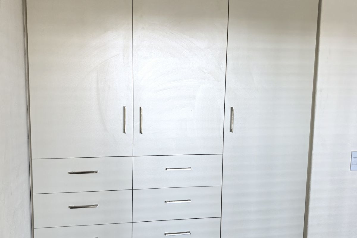 A bedroom featuring a large, floor-to-ceiling built-in wardrobe with integrated drawers and modern laminate flooring.