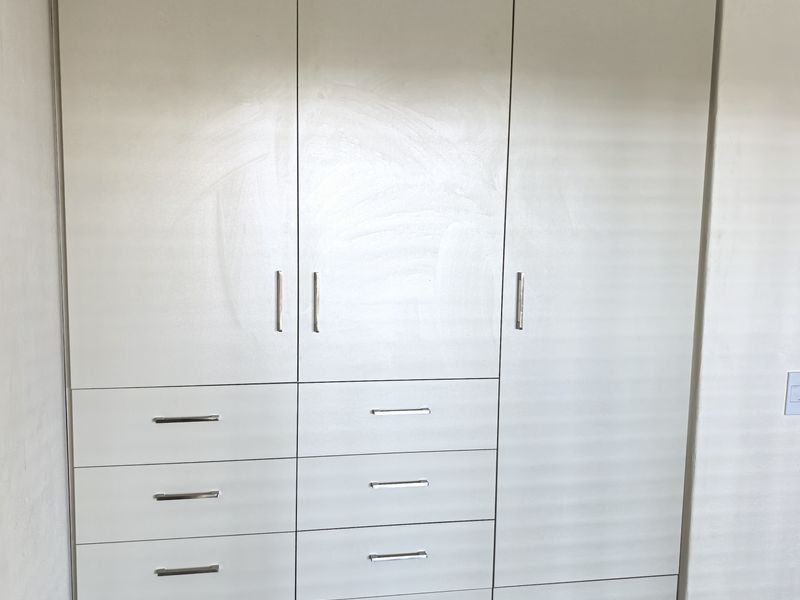 A bedroom featuring a large, floor-to-ceiling built-in wardrobe with integrated drawers and modern laminate flooring.