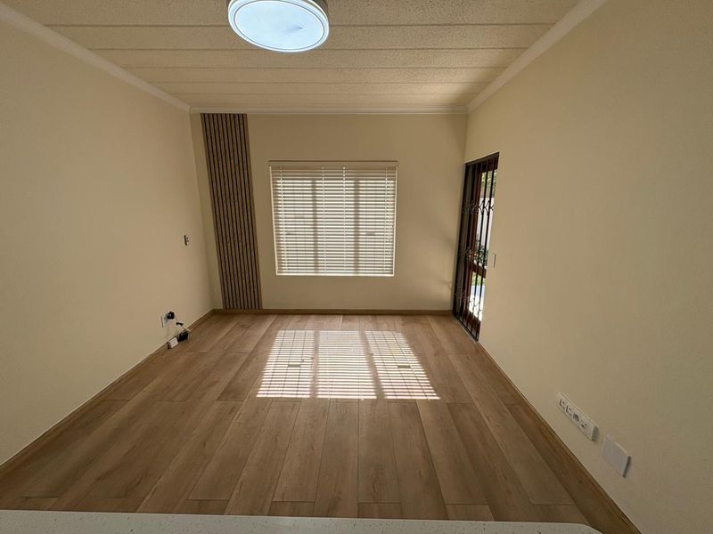 A bright, empty living room featuring modern laminate flooring, slatted wood accent wall paneling, and a security gate leading to the exterior.