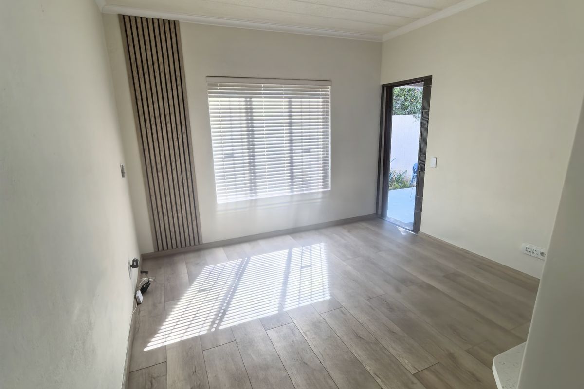 Bright and empty living area featuring wood-look laminate flooring, modern slatted wall paneling, and a ceiling fan, with direct access to an outdoor space.