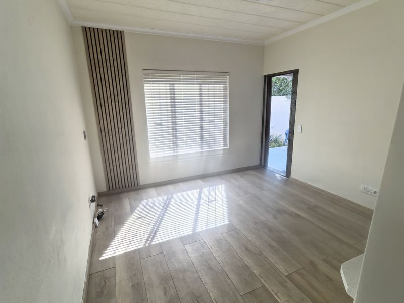 Bright and empty living area featuring wood-look laminate flooring, modern slatted wall paneling, and a ceiling fan, with direct access to an outdoor space.