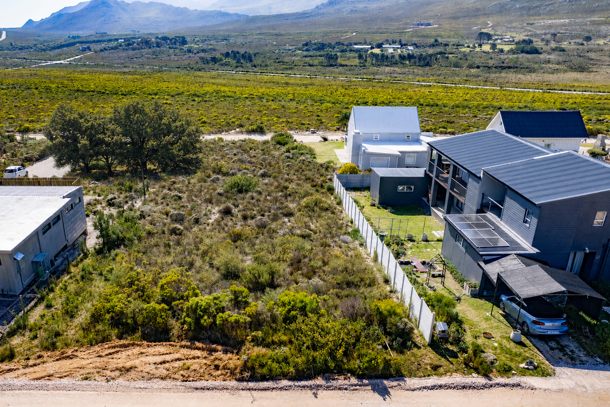 Aerial view of a vacant residential plot featuring natural vegetation, adjacent to existing residential properties with established fencing and solar infrastructure.