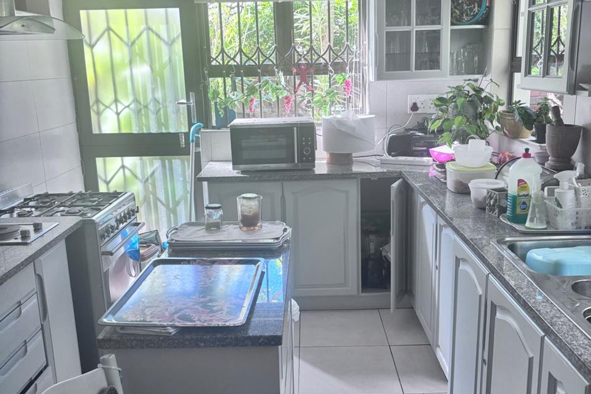 A functional kitchen featuring granite countertops, built-in cabinetry, a gas stove with extractor fan, and tiled flooring, with direct access to the exterior.