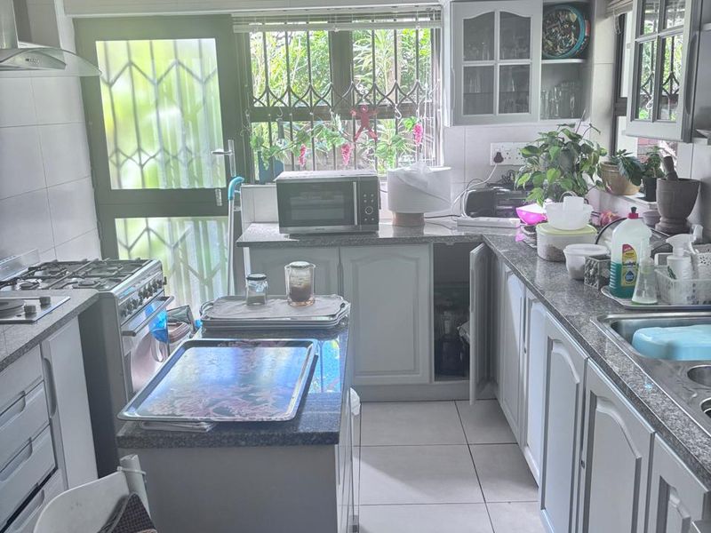 A functional kitchen featuring granite countertops, built-in cabinetry, a gas stove with extractor fan, and tiled flooring, with direct access to the exterior.