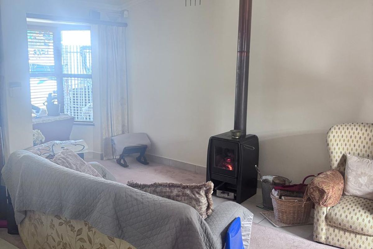 A living room featuring a freestanding fireplace with a flue pipe, crown molding, and a combination of tiled and carpeted flooring.