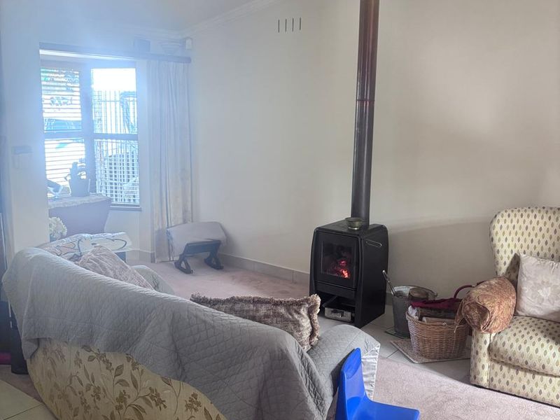 A living room featuring a freestanding fireplace with a flue pipe, crown molding, and a combination of tiled and carpeted flooring.