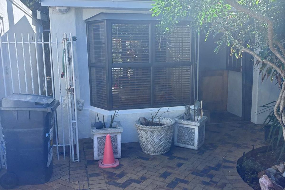 A rear exterior view of the property featuring brick paving, a bay window, and metal security fencing.
