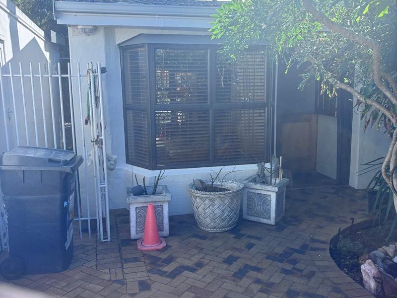 A rear exterior view of the property featuring brick paving, a bay window, and metal security fencing.