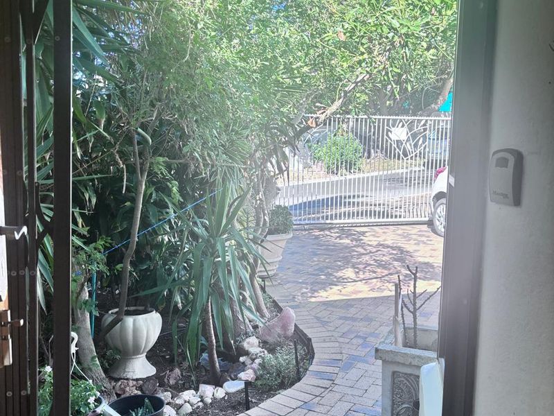 View from the entrance looking out towards the paved driveway and security gate, surrounded by established garden greenery.