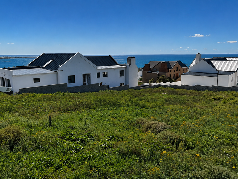 A scenic view overlooking a vacant residential plot with established coastal homes and a clear ocean horizon in the background.