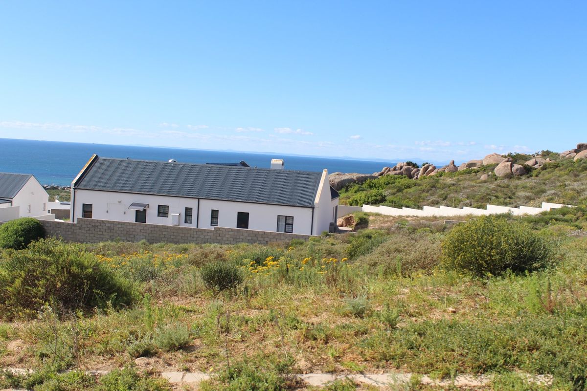 A view of a residential property featuring a white building with a dark metal roof, set against a coastal landscape with ocean views.