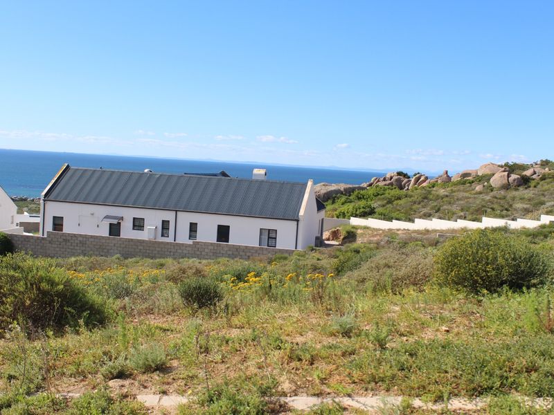 A view of a residential property featuring a white building with a dark metal roof, set against a coastal landscape with ocean views.