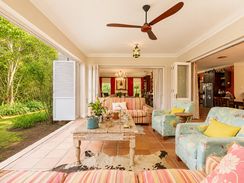 Spacious covered patio featuring terracotta flooring, ceiling fan, and large folding glass doors that open seamlessly to the lush garden.