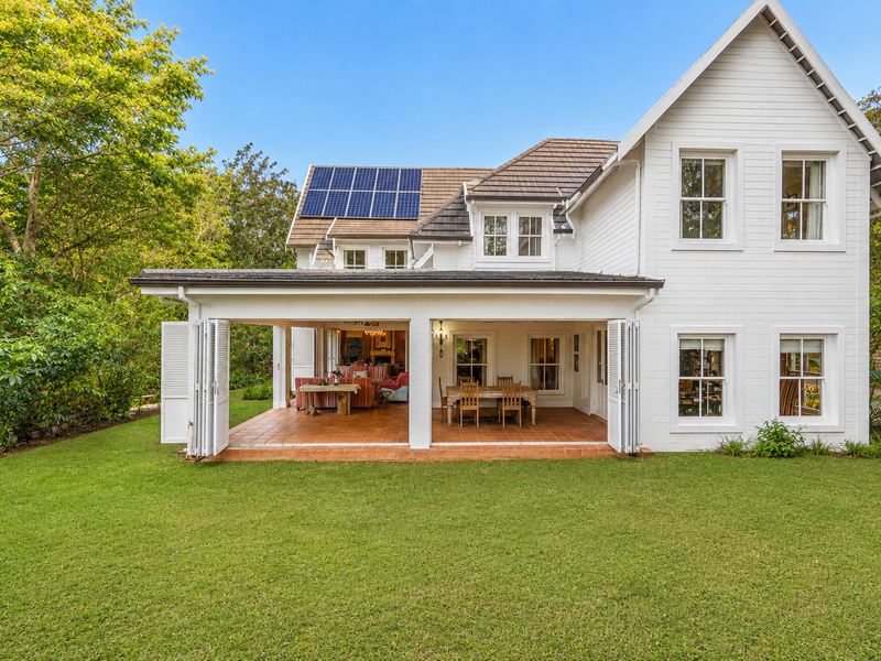A well-maintained rear elevation featuring a spacious covered patio with bi-fold doors, sash windows, and roof-mounted solar panels overlooking a lush garden.