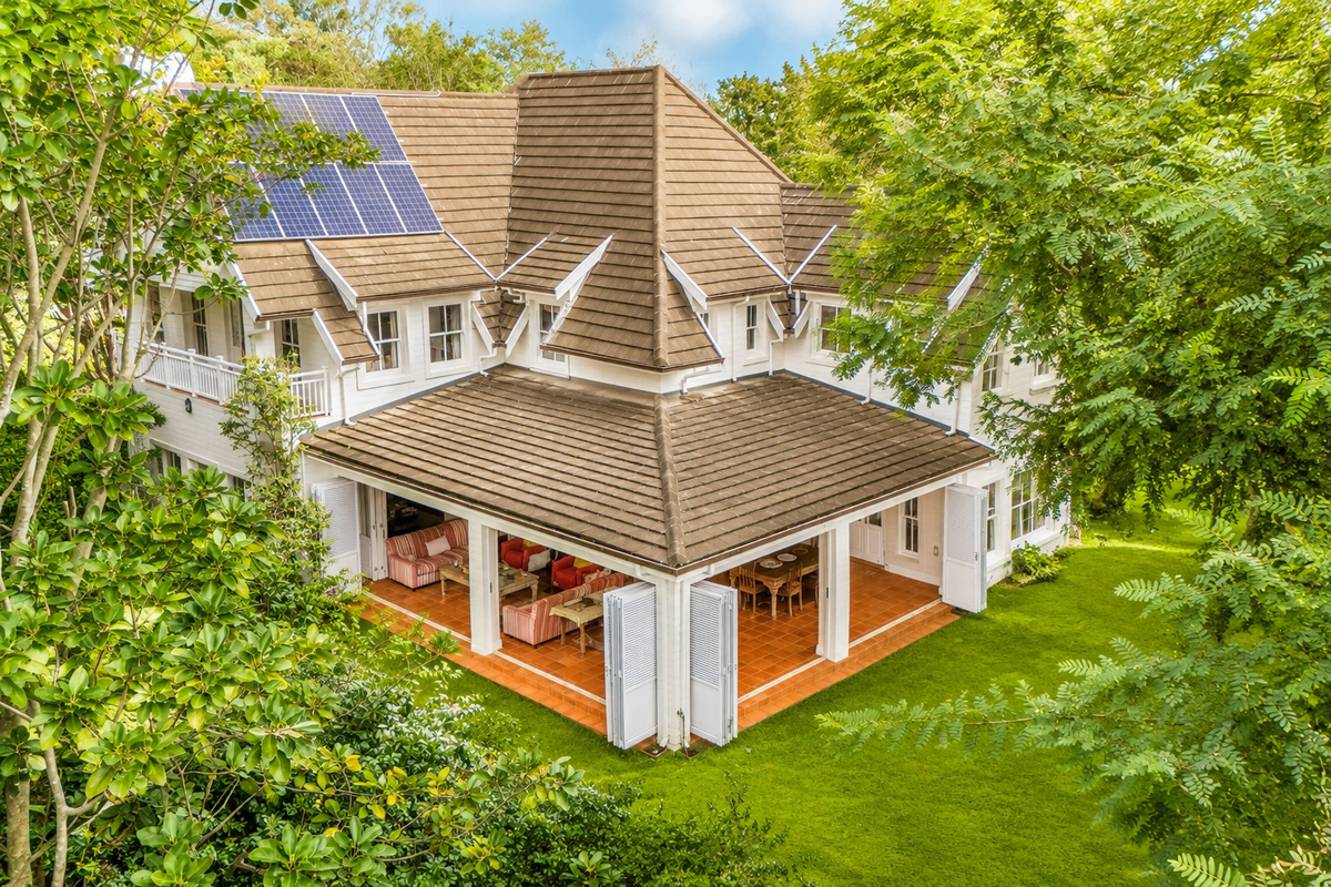 Aerial view of a well-maintained two-story house featuring a tiled roof, solar panels, and a spacious covered patio opening onto a lush garden.