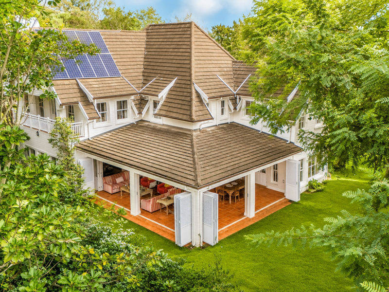 Aerial view of a well-maintained two-story house featuring a tiled roof, solar panels, and a spacious covered patio opening onto a lush garden.