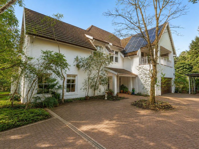 A well-maintained two-story house featuring a brick facade, tiled roof, solar panels, and a spacious paved driveway with mature garden surroundings.