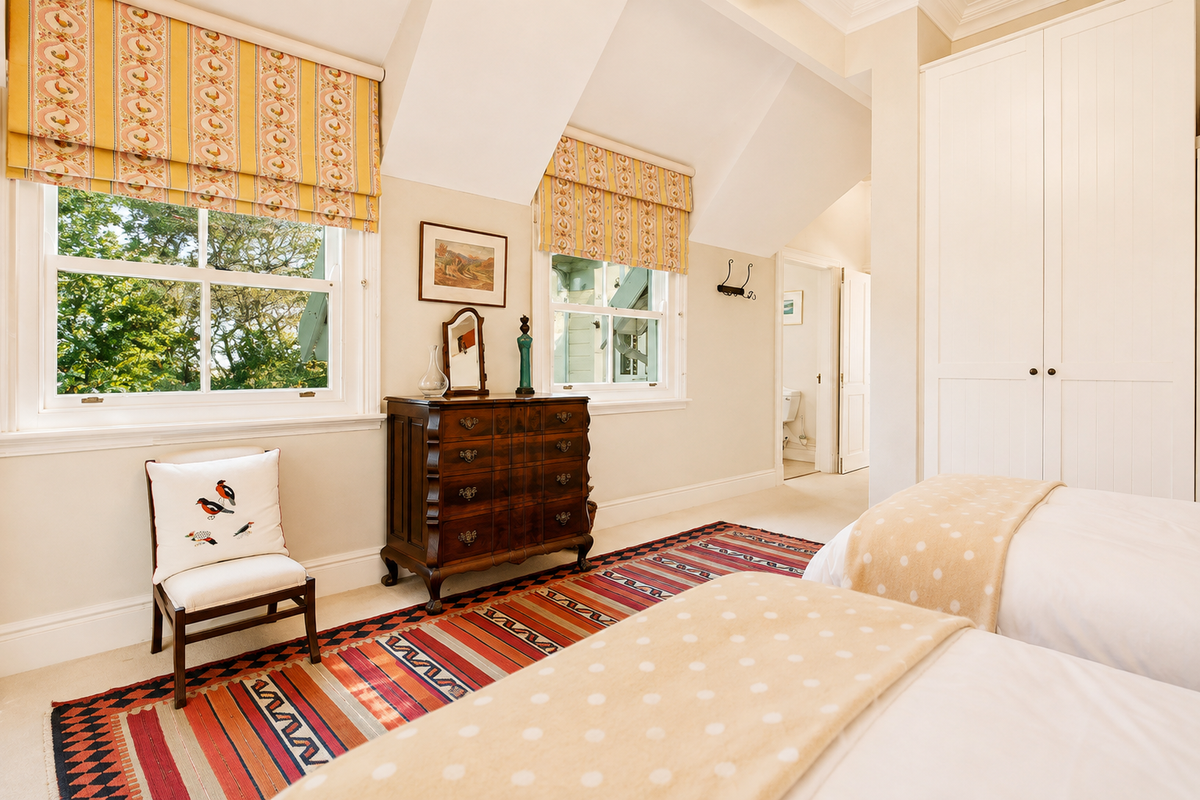 A well-maintained bedroom featuring built-in wardrobes, classic sash windows with patterned blinds, and neutral carpeting, offering a bright and comfortable living space.