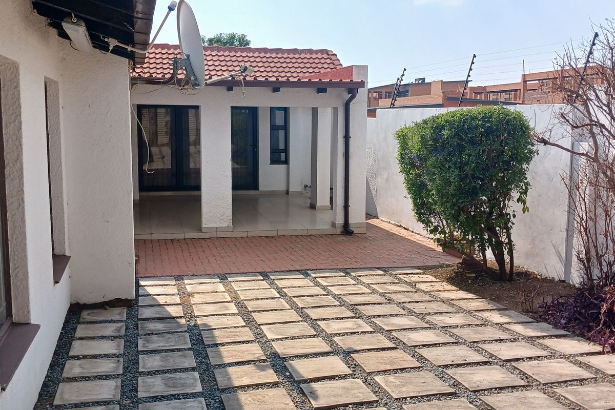 A rear exterior view featuring a covered patio area, paved courtyard, and a secure boundary wall with electric fencing.