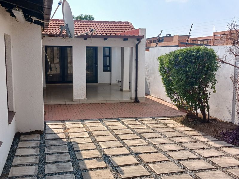 A rear exterior view featuring a covered patio area, paved courtyard, and a secure boundary wall with electric fencing.