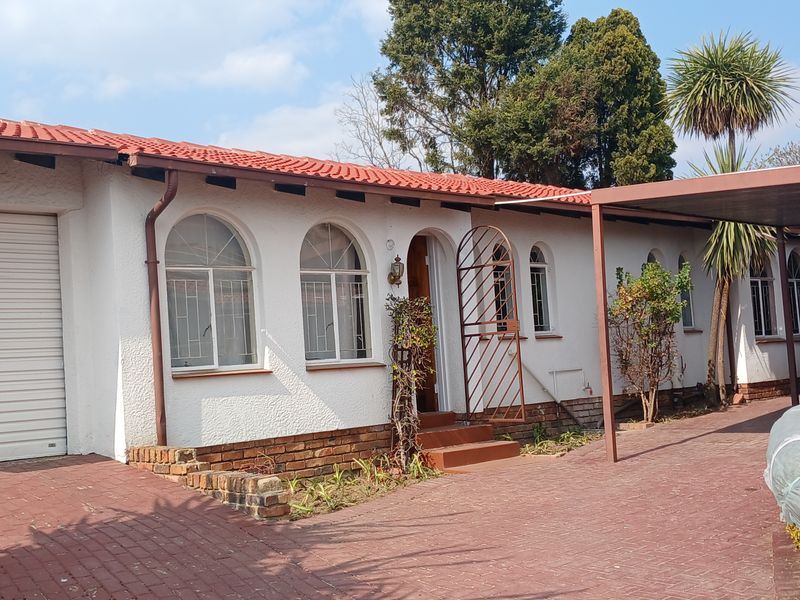 Front elevation of a single-story house featuring a tiled roof, arched windows with security bars, a roller garage door, and a paved driveway with carport.