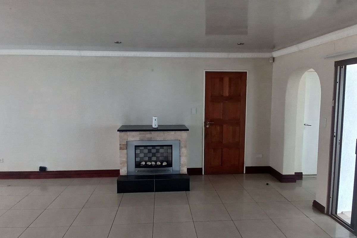 Spacious living room featuring tiled flooring, a built-in fireplace, and sliding glass doors with security gates leading to the exterior.