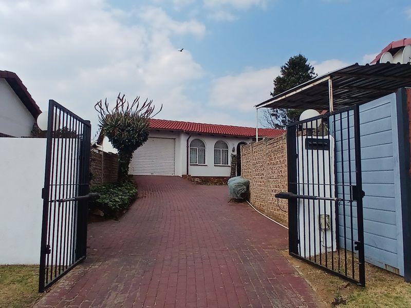 Front view of the property featuring a paved driveway, metal security gate, brick boundary walls, and a garage with a tiled roof.